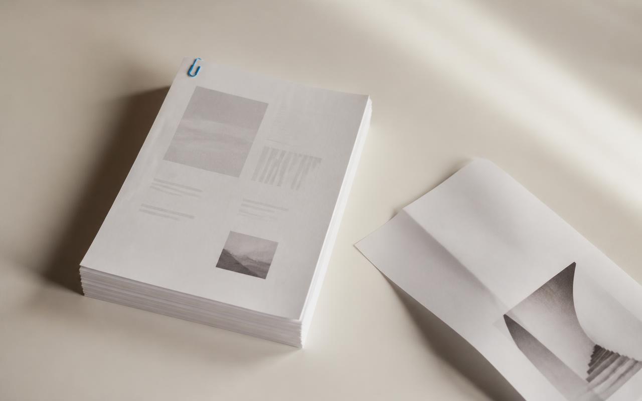 A plain stack of printed documents and a folded sheet of paper resting on a warm porcelain surface